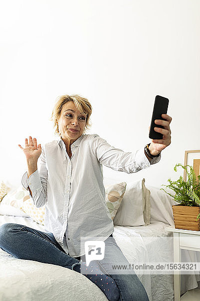 Reife Frau  die zu Hause auf dem Bett sitzt und ein Selfie