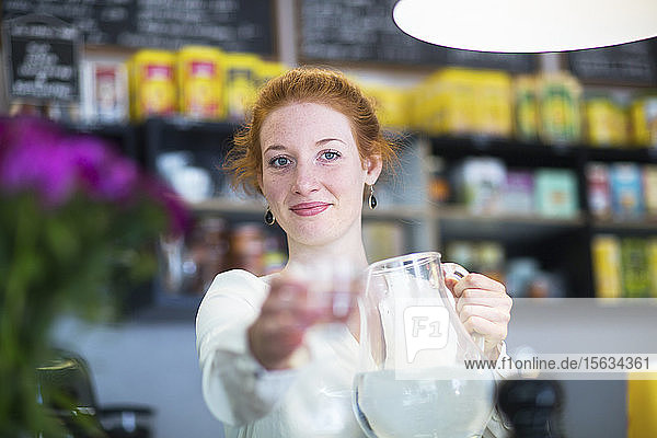 Junge Frau  die im Café arbeitet und ein Wasserglas schenkt