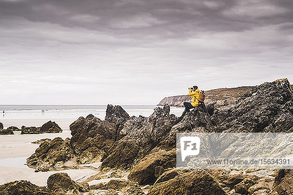 Young woman wearing yellow rain jacket at the beach  looking through binoculars  Bretagne  France
