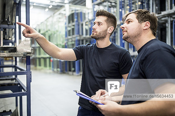 Worker with colleague in factory warehouse pointing his finger