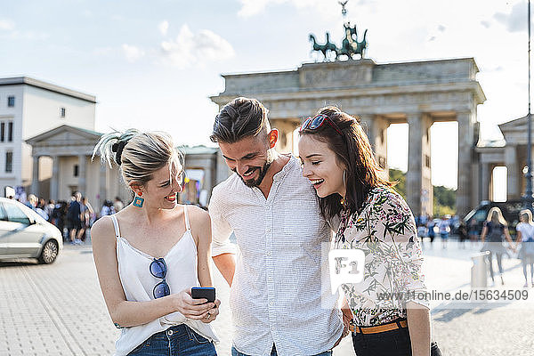 Drei Freunde schauen auf Handy vor dem Brandenburger Tor  Berlin  Deutschland