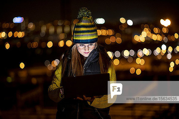 Junge Frau  die nachts im Freien einen Laptop benutzt