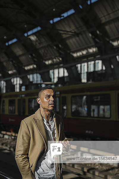 Porträt eines Geschäftsmannes  der mit Smartphone und Kopfhörern am Bahnhof steht  Berlin  Deutschland