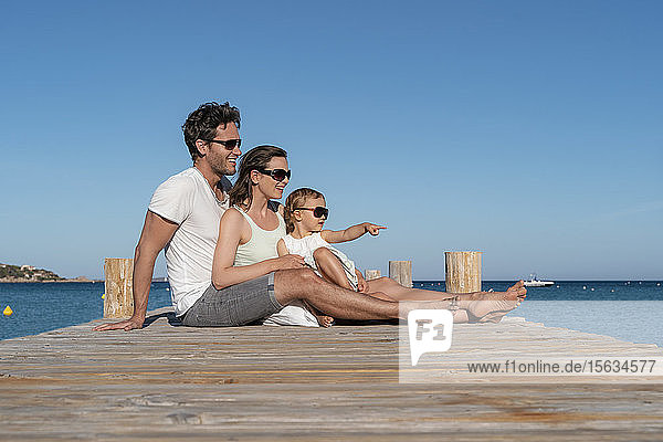 Glückliche Familie sitzt auf einem Steg am Meer