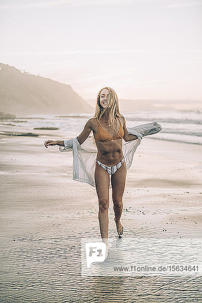 Junge blonde Frau im Bikini am Strand bei Sonnenaufgang