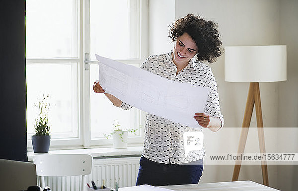 Smiling young woman studying a plan in office