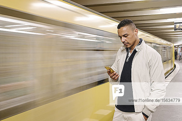 Porträt eines Mannes  der vor einem fahrenden U-Bahn-Zug steht und auf sein Handy schaut  Berlin  Deutschland