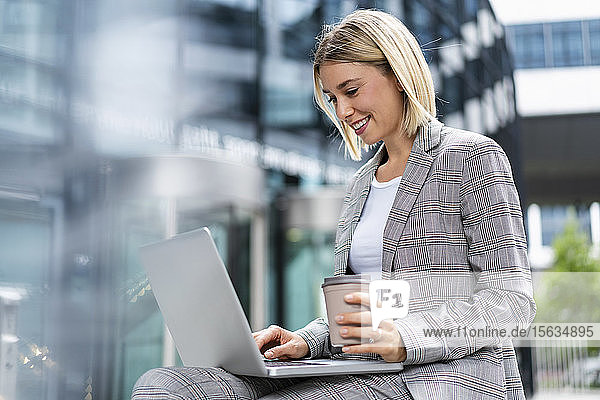 Smiling young businesswoman using laptop in the city