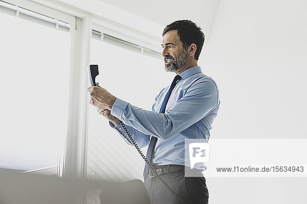 Angry mature businessman holding telephone receiver in office