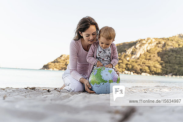 Mutter und kleine Tochter schauen gemeinsam auf den Strandball der Erde