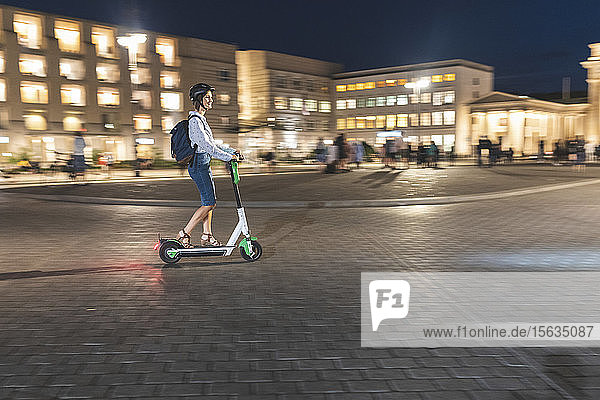 Young woman riding an electric scooter on 'Pariser Platz' at night  Berlin  Germany