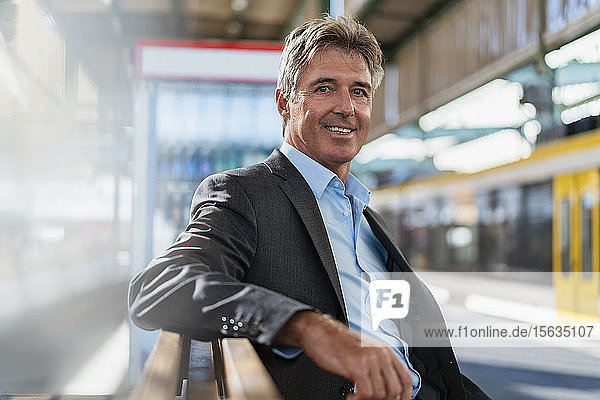 Porträt eines lächelnden reifen Geschäftsmannes  der am Bahnsteig wartet
