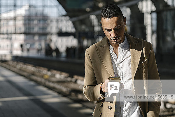 Geschäftsmann steht mit einem Smartphone auf dem Bahnsteig des Bahnhofs Alexanderplatz  Berlin  Deutschland