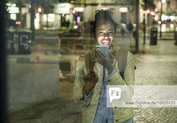 Porträt einer lachenden jungen Frau am Telefon in der Stadt bei Nacht Lissabon Portugal
