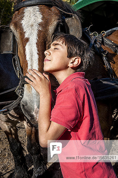 Boy with closed eyes hugging a horse