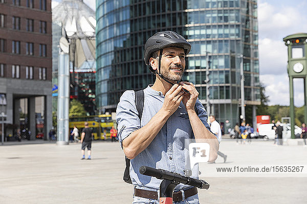 Man fastening the helmet before riding on electric scooter  Berlin  Germany