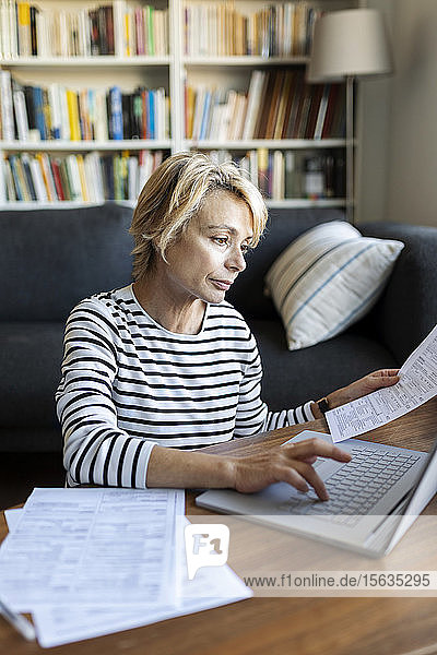 Reife Frau mit Dokumenten  die zu Hause einen Laptop benutzen