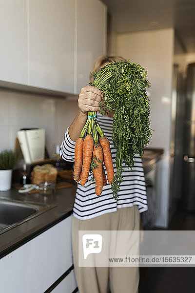 Frau hält zu Hause in der Küche einen Karottenstrauss