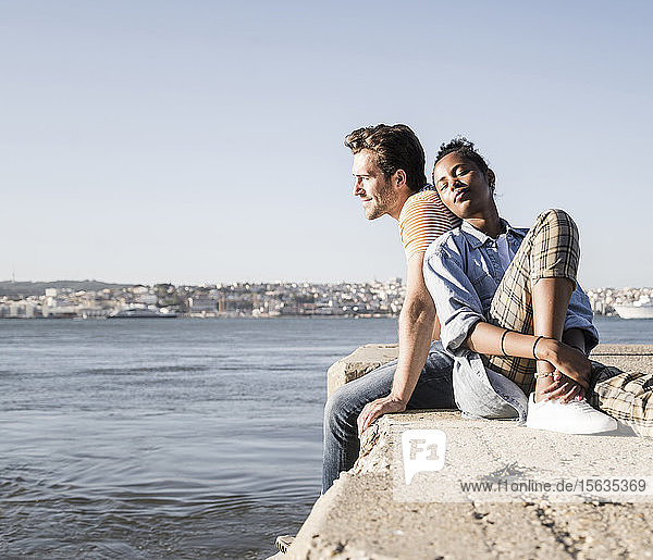 Young couple sitting on pier at the waterfront  Lisbon  Portugal