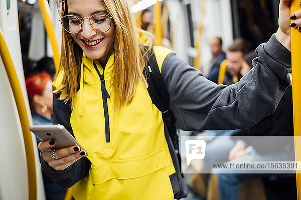 Smiling young woman standing in underground train using her smartphone