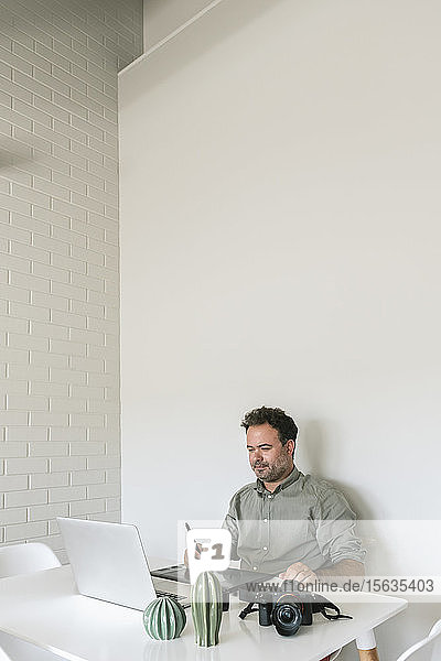 Porträt eines Mannes  der am Tisch sitzt und an Grafiktablett und Laptop arbeitet
