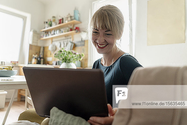 Portrait of happy woman sitting in the kitchen using laptop