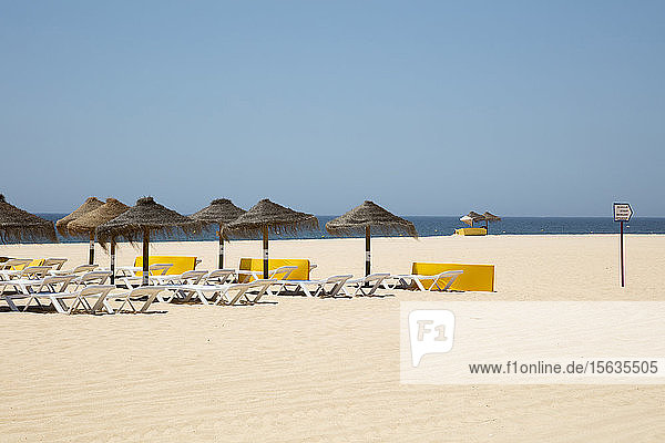 Sonnenschirme und Liegestühle mit Reetdach am Sandstrand vor klarem Himmel  Albufeira  Algarve  Portugal