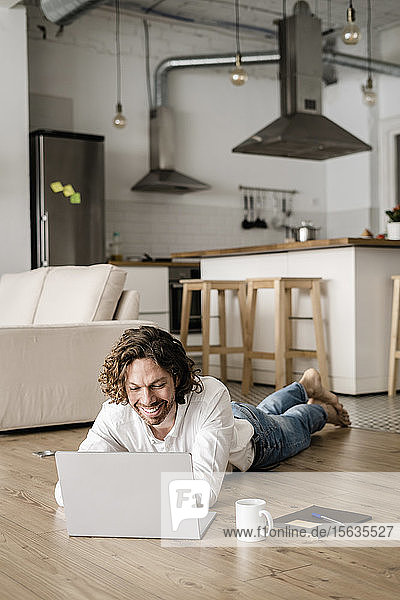 Lächelnder Mann liegt zu Hause mit Laptop auf dem Boden