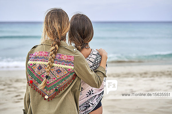 Rear view of two young women standing close to each other on a beach