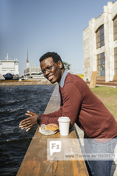 Junger Mann schaut auf das Meer  mit Hamburger und Kaffee an der Reling
