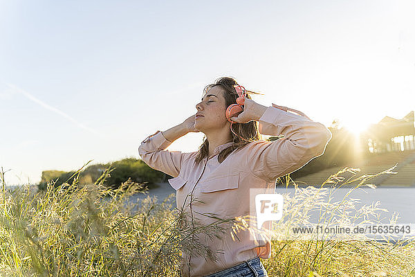 Junge Frau mit geschlossenen Augen  die im Freien mit Kopfhörern Musik hört