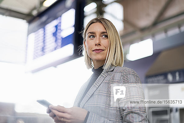 Junge Geschäftsfrau mit Mobiltelefon am Bahnhof