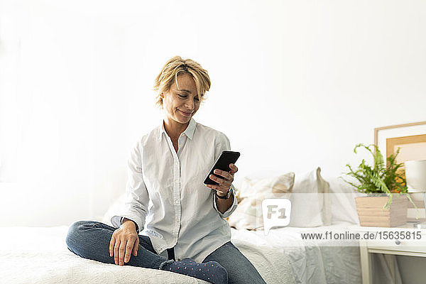 Reife Frau sitzt zu Hause im Bett und benutzt ein Smartphone