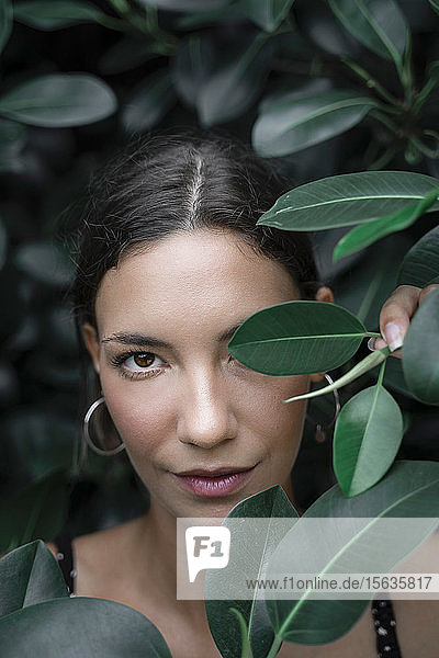Porträt einer jungen Frau  die sich hinter grünen Blättern versteckt