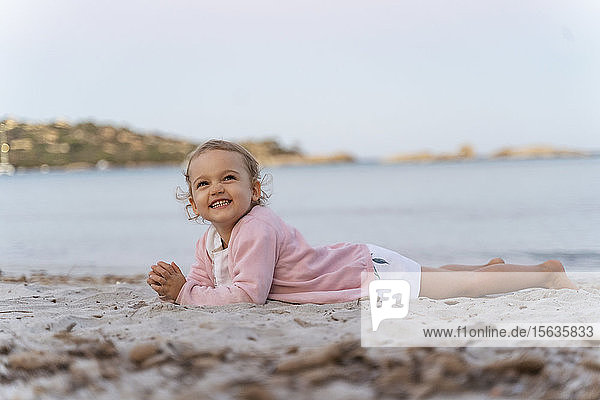 Glückliches süßes Kleinkind am Strand liegend