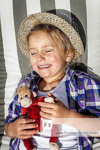 Little girl with cuddly toy lying in sunshine