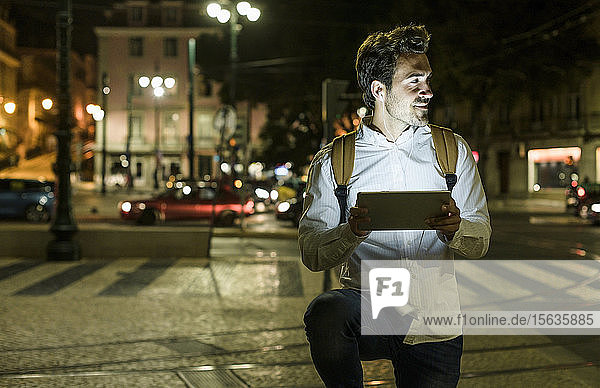 Portrait of young man using cell phone and earphones in the city by night  Lisbon  Portugal