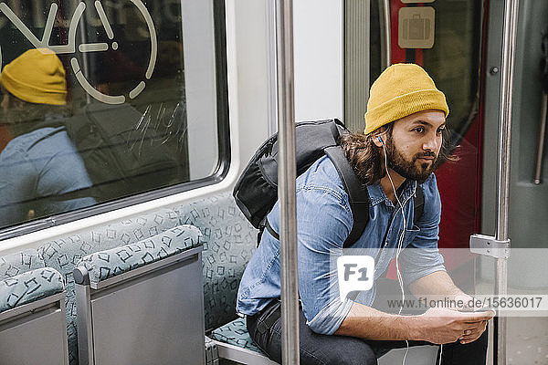 Mann mit Rucksack beim Musikhören mit Smartphone und Kopfhörern in Pendlerlinie  Berlin  Deutschland
