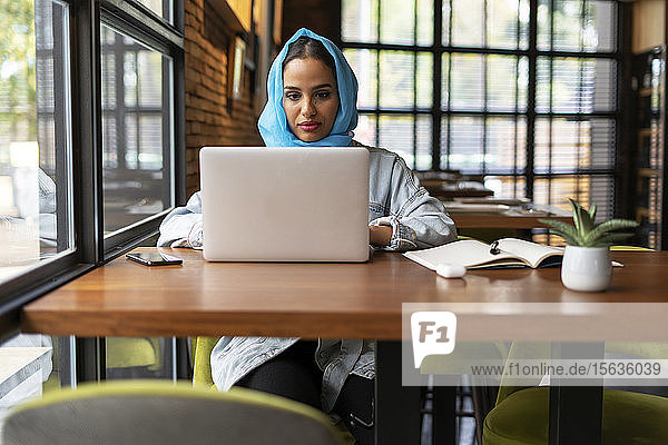 Businesswoman wearing turquoise hijab in a cafe and working  using laptop