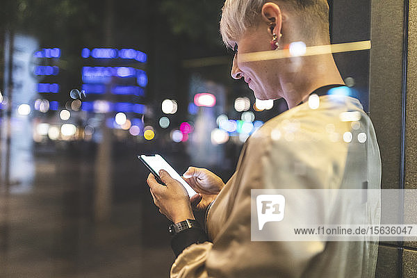 Smiling blond woman using mobile phone in the city at night  Berlin  Germany