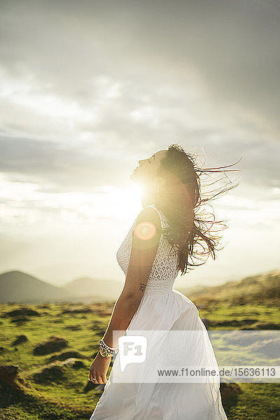 Junge Frau in weißem Kleid auf Aussichtspunkt bei Sonnenuntergang
