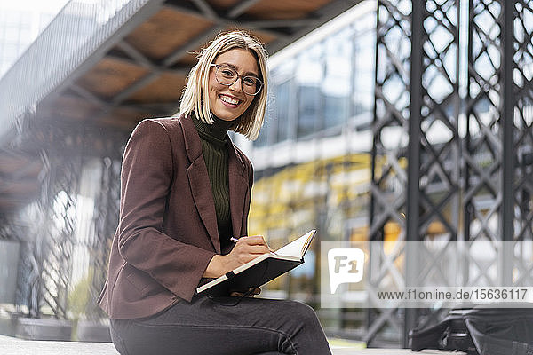 Porträt einer glücklichen jungen Geschäftsfrau mit Notizbuch in der Stadt