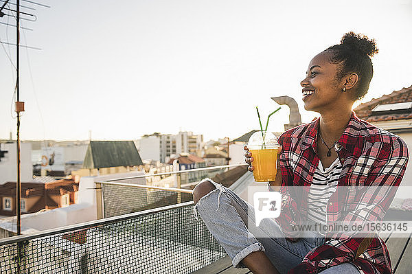 Glückliche junge Frau trinkt bei Sonnenuntergang auf dem Dach