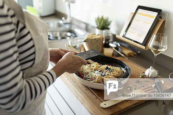 Nahaufnahme einer Frau  die ein Smartphone-Foto von ihrem Nudelgericht in der heimischen Küche macht