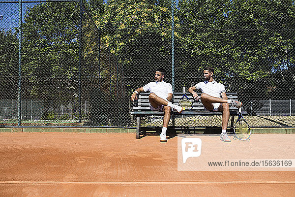 Tennis players sitting on a bench during break and looking sideways