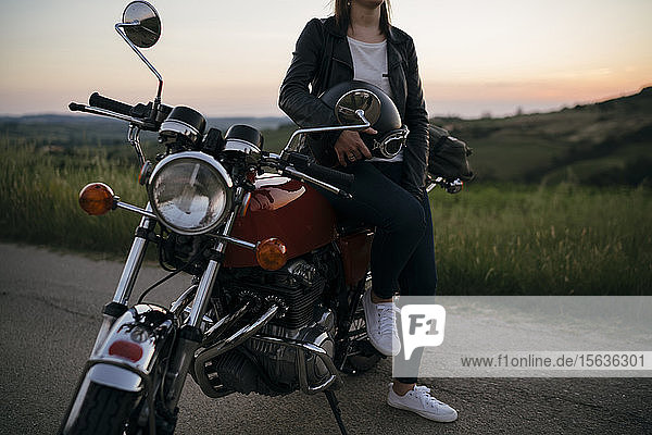 Schnappschuss einer jungen Frau mit einem Oldtimer-Motorrad auf einer Landstraße bei Sonnenuntergang  Toskana  Italien
