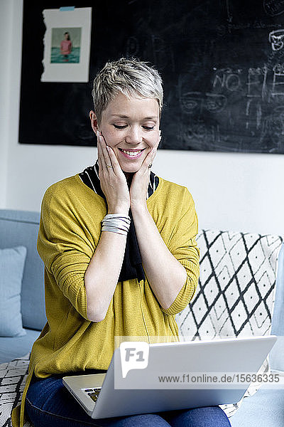 Porträt einer glücklichen Frau  die auf der Couch sitzt und auf den Laptop schaut