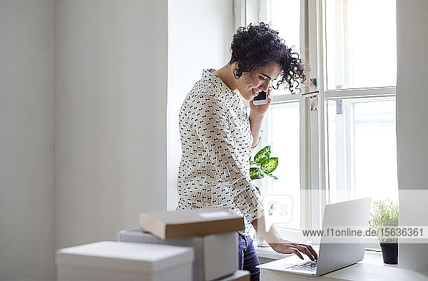 Smiling young woman on the phone using laptop in home office
