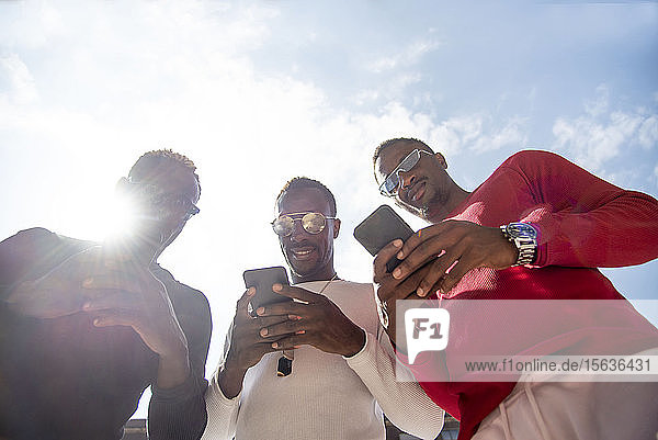 Drei coole junge Männer mit Mobiltelefonen im Gegenlicht