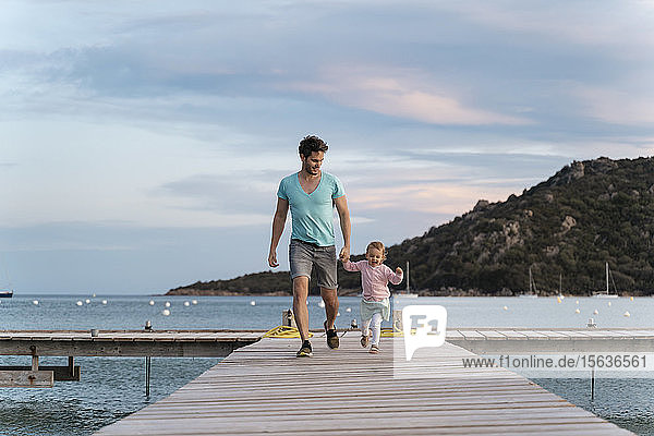 Glücklicher Vater geht mit seiner Tochter bei Sonnenuntergang auf einem Steg